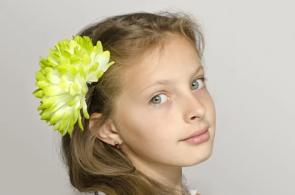 Mooie jonge blonde meisje in witte jurk glimlachen, portret van een schattig jong geitje. Meisje met een groene grote bloem in haar haar, ruiken een bloem — Stockfoto