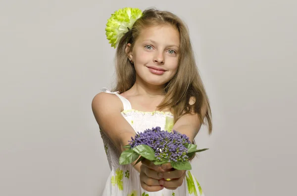 Mooie jonge blonde meisje in witte jurk glimlachen, portret van een schattig jong geitje. Meisje met een groene grote bloem in haar haar, ruiken een bloem — Stockfoto