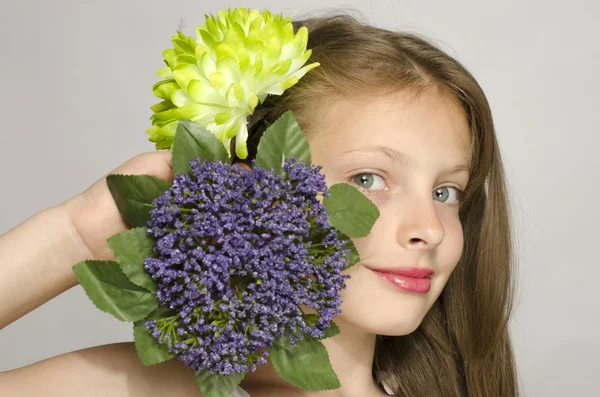 Beautiful young blonde girl in white dress smiling, portrait of an adorable kid. Little girl with a green big flower in her hair, smelling a flower — Stock Photo, Image