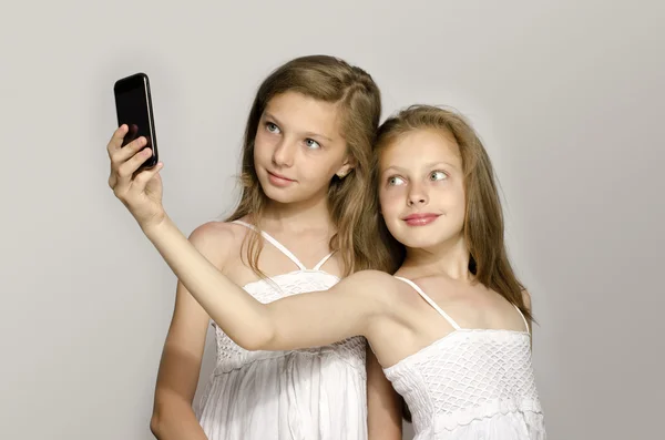 Två unga flicka med en selfie, barnen ta ett foto och ha roligt, flickor leker med en mobiltelefon — Stockfoto