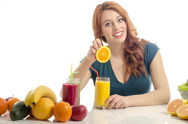 幸せな女は、有機食品、ジュース、スムージーの完全なテーブルを持っています。陽気な若い女性の健康的なサラダや果物を食べるします。白で隔離。女性を絞るとオレンジと有機ジュースを準備 — ストック写真