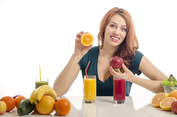 Mujer feliz teniendo una mesa llena de comida orgánica, jugos y batidos. Joven alegre comiendo ensalada saludable y frutas. Aislado sobre blanco. Mujer exprimiendo y naranja y preparando un jugo orgánico —  Fotos de Stock