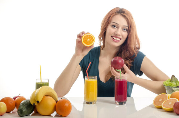 Happy woman having a table full of organic food,juices and smoothie. Cheerful young woman eating healthy salad and fruits. Isolated on white. Woman squeezing and orange and preparing an organic juice