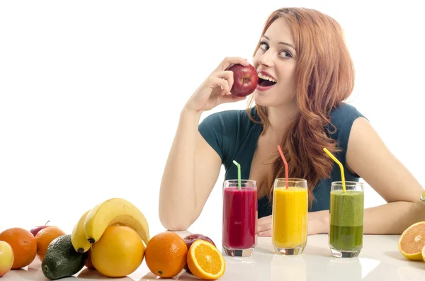 Szczęśliwa kobieta o stół pełne żywności ekologicznej, soki i koktajl. Wesoły młoda kobieta jedzenie zdrowe sałatki i owoce. Na białym tle. Dziewczynka jedzenie świeże czerwone jabłko. — Zdjęcie stockowe