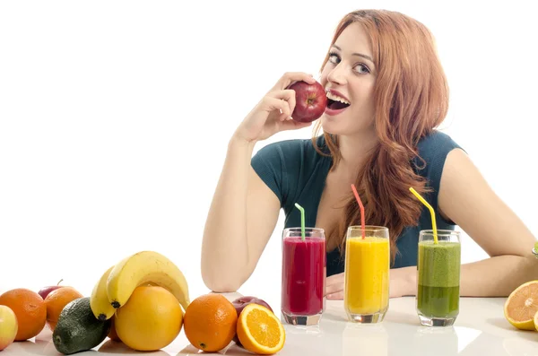 Gelukkige vrouw met een tafel vol met biologisch voedsel, sappen en smoothie. Vrolijke jonge vrouw eten gezonde salade en fruit. Geïsoleerd op wit. Meisje een verse rode appel eten. — Stockfoto