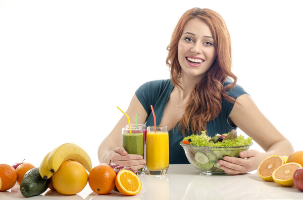 Happy woman having a table full of organic food,juices and smoothie. Cheerful young woman eating healthy salad and fruits. Isolated on white