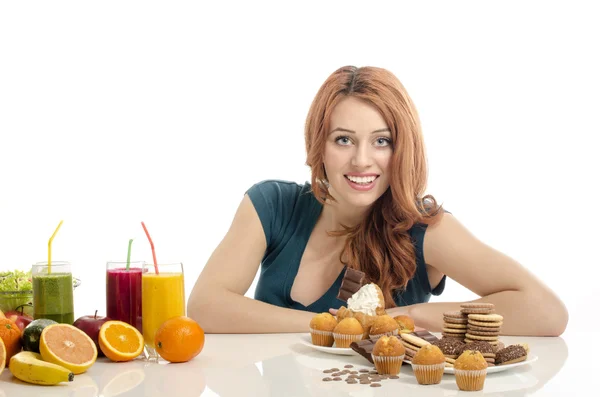 Woman choosing between fruits, smoothie and organic healthy food against sweets, sugar, lots of candies, unhealthy food. Treating your sweets addiction with fruits and vegetables — Stock Photo, Image