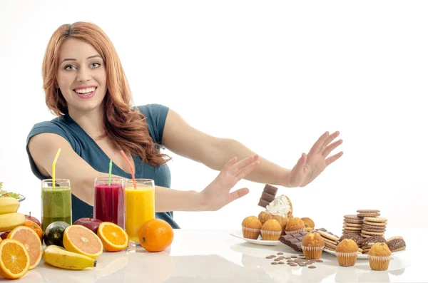 Woman choosing between fruits, smoothie and organic healthy food against sweets, sugar, lots of candies, unhealthy food. Treating your sweets addiction with fruits and vegetables — Stock Photo, Image