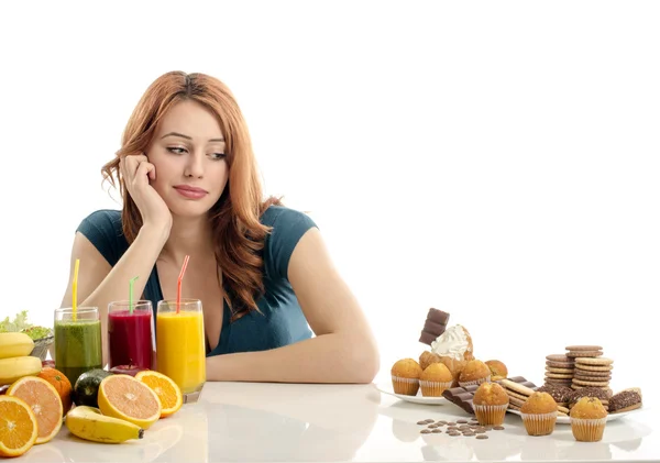 Vrouw kiezen tussen fruit smoothie en organische gezonde voeding tegen snoep, suiker, veel snoepjes, ongezond voedsel. Behandeling van uw verslaving snoepjes met groenten en fruit — Stockfoto