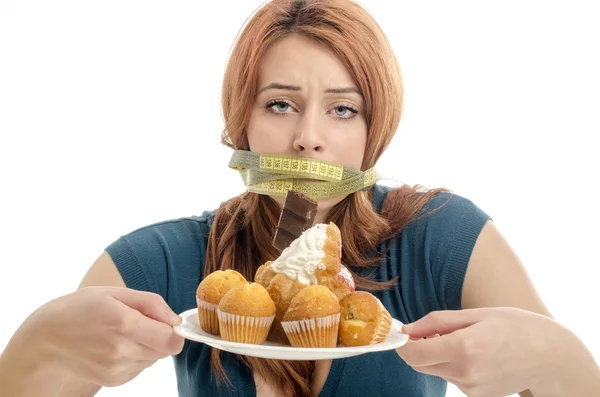 Mujer con un centímetro en la boca incapaz de comer todos los dulces y el azúcar, un montón de galletas en un plato. Dieta sin dulces —  Fotos de Stock