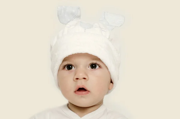天真的孩子戴着白色的帽子，看起来很可爱。孩子穿的冬天，可爱的新生儿。可爱的宝宝画像看好奇。宝宝打扮成有趣的兔子，戴着白色帽子的兔子耳朵 — 图库照片