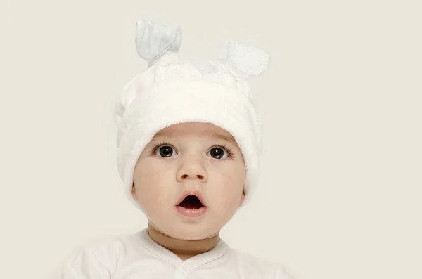 Bébé innocent portant un chapeau blanc à l'air adorable. Enfant habillé pour l'hiver, beau nouveau-né. Adorable portrait de bébé à l'air curieux. Bébé habillé comme un lapin drôle avec un chapeau blanc avec des oreilles de lapin — Photo