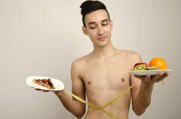 Man choosing between fruits, organic healthy food against pizza, fast food. Skinny anorexic man dieting and choosing what is healthy for him — Stock Photo, Image