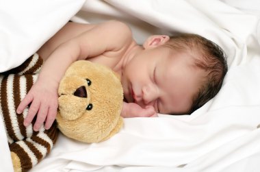 Güzel masum yeni doğan uyuyor. Beyaz çarşaf bir banyodan sonra rahatlatıcı ve ona yakın tutmak onun ayı oyuncak sevimli küçük çocuk. Oyuncak ayı küçük bebek korumak