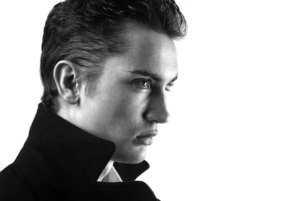 Profil eines schönen jungen Mannes in einem schwarzen langen Mantel, der Mode posiert — Stockfoto