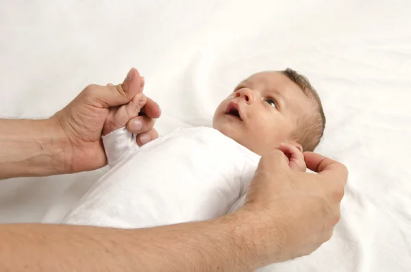 Um lindo recém-nascido inocente a olhar para o pai. Menino adorável relaxando e brincando em lençóis brancos depois de um banho, as mãos do pai segurando seu recém-nascido com amor — Fotografia de Stock