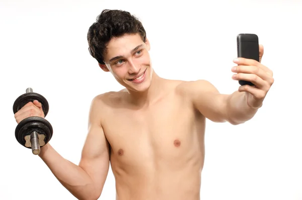 瘦男人同时训练他的二头肌肌肉以用他的手机拍照。美丽的少年举哑铃、 拍照的 facebook。厌食症的年轻男子，训练变得更强 — 图库照片