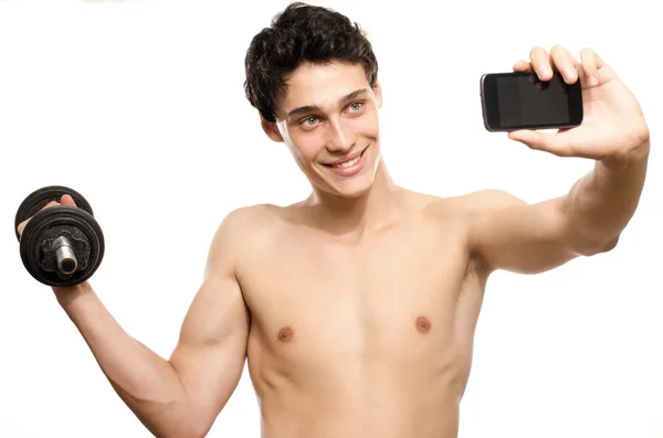 Skinny man taking a selfie with his phone while training his bicep muscle. Beautiful teenager lifting a dumbbell and taking a photo for facebook.Anorexic young man training to become stronger — Stock Photo, Image