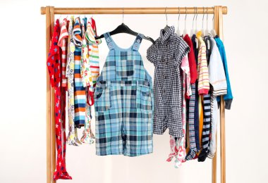 Dressing closet with clothes arranged on hangers.Colorful wardrobe of newborn,kids, toddlers, babies on a rack.Many t-shirts,pants, shirts,blouses, onesie hanging
