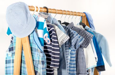 Soyunma dolap askı düzenlenmiş giysileri ile. Yeni doğmuş bebek, çocuk, küçük çocuklar, bebekler tüm giysiler tam mavi ve beyaz gardırop. Birçok t-gömlek, pantolon, gömlek, bluz, mavi şapka, asılı onesie