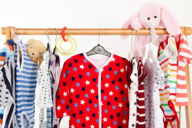 Soyunma dolap askı düzenlenmiş giysileri ile. Yeni doğan, çocuklar, yeni yürümeye başlayan çocuklar, bebekler tüm giysiler tam renkli gardırop. Birçok t-gömlek, pantolon, gömlek, bluz, onesie asılı, ayı ve tavşan oyuncak