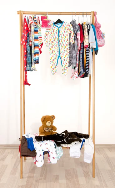 Dressing closet with clothes arranged on hangers.Colorful wardrobe of newborn,kids, toddlers, babies on a rack.Many t-shirts,pants, shirts,blouses, onesie hanging. Messy clothes thrown on a shelf — Stock Photo, Image
