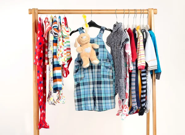 Dressing closet with clothes arranged on hangers.Colorful wardrobe of newborn,kids, toddlers, babies on a rack.Many t-shirts,pants, shirts,blouses, onesie hanging, bear toy — ストック写真