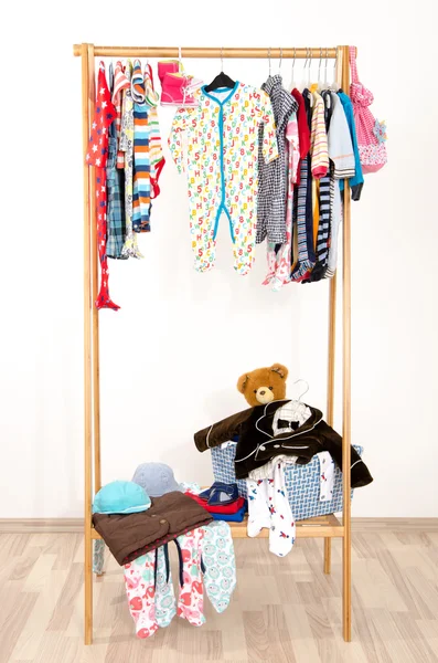 Dressing closet with clothes arranged on hangers.Colorful wardrobe of newborn,kids, toddlers, babies on a rack.Many t-shirts,pants, shirts,blouses, onesie hanging. Messy clothes thrown on a shelf — Stock Photo, Image