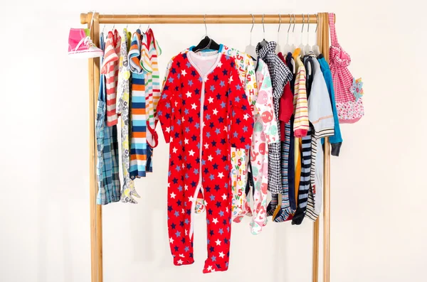 Dressing kast met kleren gerangschikt op hangers. Kleurrijke garderobe van pasgeboren kinderen, peuters, baby's vol met alle kleren. Vele t-shirts, broeken, shirts, blouses, gele hoed, schoenen, onesie opknoping — Stockfoto