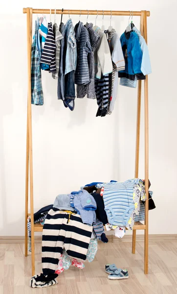 Dressing closet with clothes arranged on hangers.Wardrobe of newborn,kids, toddlers, babies.Many t-shirts,pants, shirts,blouses, shoes, onesie hanging. Messy clothes thrown on a shelf — Stock Fotó