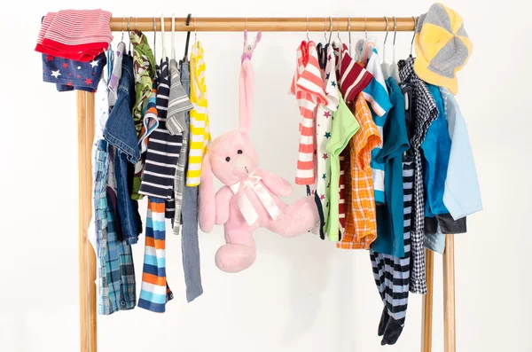 Dressing closet with clothes arranged on hangers.Colorful wardrobe of newborn,kids, toddlers, babies full of all clothes.Many t-shirts,pants, shirts,blouses, onesie on a rack, pink rabbit toy hanging — Stock Photo, Image
