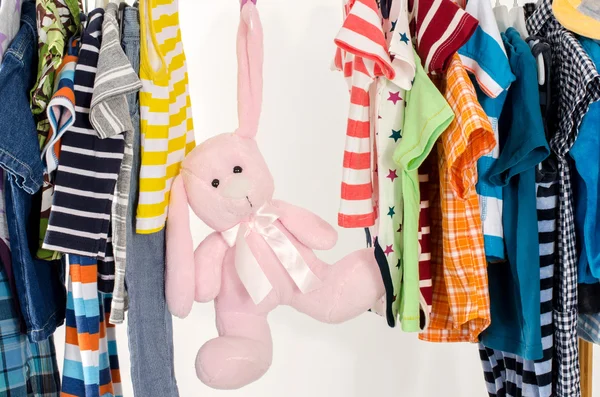 Dressing closet with clothes arranged on hangers.Colorful wardrobe of newborn,kids, toddlers, babies full of all clothes.Many t-shirts,pants, shirts,blouses, onesie on a rack, pink rabbit toy hanging — 스톡 사진