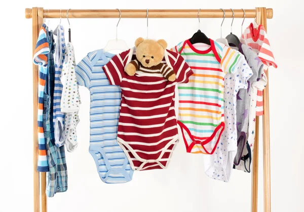 Dressing closet with clothes arranged on hangers.Colorful onesie of newborn,kids, toddlers, babies on a rack.Many colorful t-shirts, shirts,blouses, onesie hanging, bear toy — Zdjęcie stockowe