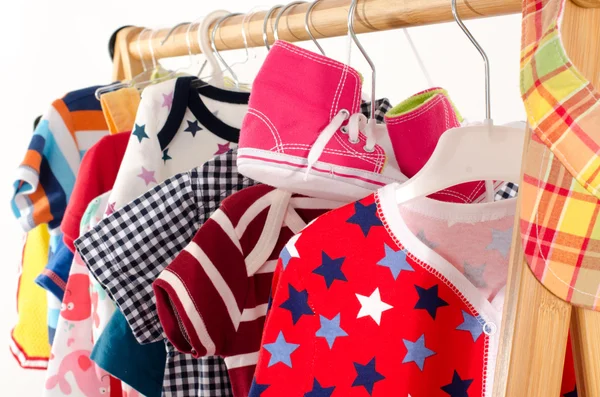 Kleiderschrank mit Kleidung auf Kleiderbügeln arrangiert.Bunte Garderobe von Neugeborenen, Kindern, Kleinkindern, Babys voller Kleidung. Viele T-Shirts, Hosen, Hemden, Blusen, gelben Hut, Schuhe, onesie hängen — Stockfoto