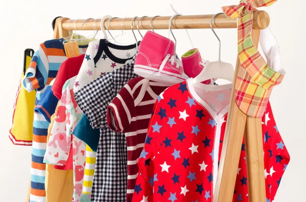 Kleiderschrank mit Kleidung auf Kleiderbügeln arrangiert.Bunte Garderobe von Neugeborenen, Kindern, Kleinkindern, Babys voller Kleidung. Viele T-Shirts, Hosen, Hemden, Blusen, gelben Hut, Schuhe, onesie hängen — Stockfoto