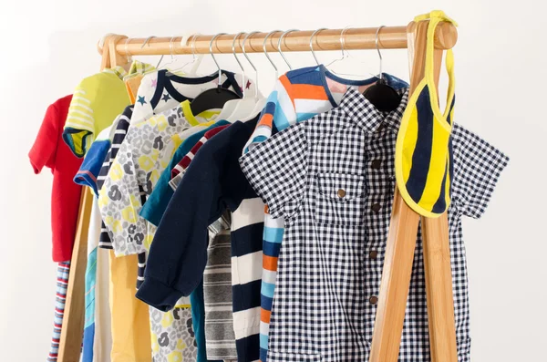 Dressing closet with clothes arranged on hangers.Colorful wardrobe of newborn,kids, toddlers, babies full of all clothes.Many t-shirts,pants, shirts,blouses,yellow hat, onesie hanging — Stock Fotó