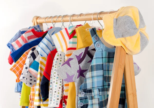 Kleiderschrank mit Kleidern auf Kleiderbügeln arrangiert.Bunte Garderobe von Neugeborenen, Kindern, Kleinkindern, Babys voller Kleidung. Viele T-Shirts, Hosen, Hemden, Blusen, gelben Hut, Onesie hängen — Stockfoto