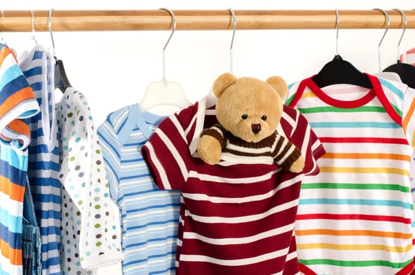 Dressing closet with clothes arranged on hangers.Colorful onesie of newborn,kids, toddlers, babies on a rack.Many colorful t-shirts, shirts,blouses, onesie hanging, bear toy Stockfoto