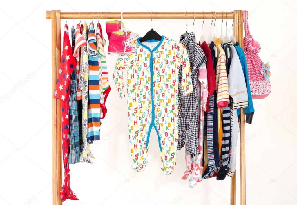 Dressing closet with clothes arranged on hangers.Colorful wardrobe of newborn,kids, toddlers, babies full of all clothes.Many t-shirts,pants, shirts,blouses,yellow hat,shoes, onesie hanging