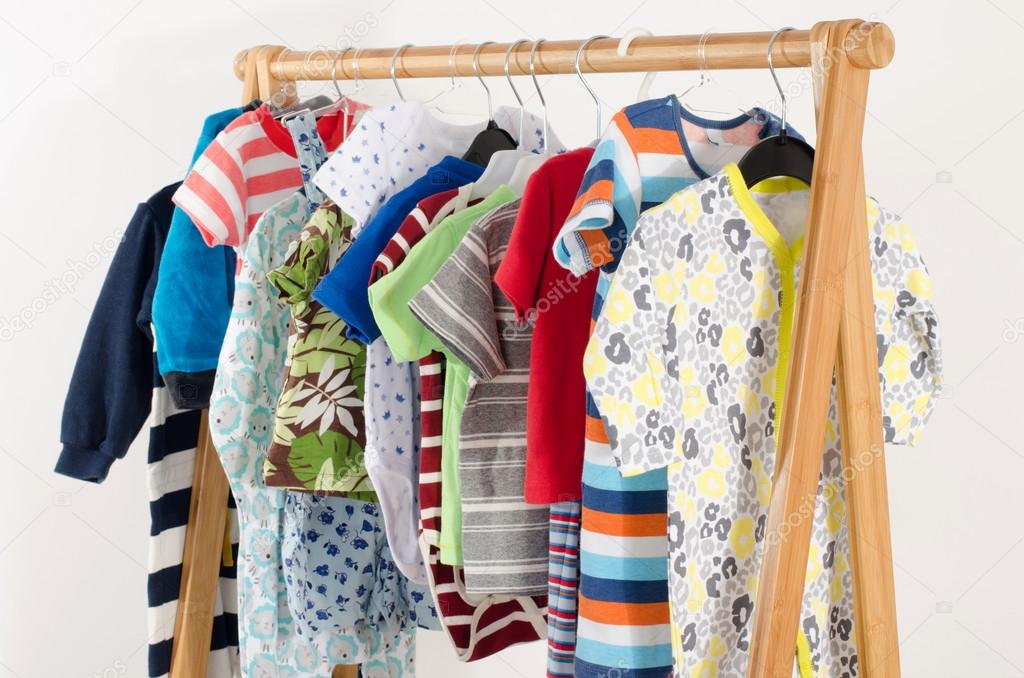 Dressing closet with clothes arranged on hangers.Colorful wardrobe of newborn,kids, toddlers, babies full of all clothes.Many t-shirts,pants, shirts,blouses, onesie hanging