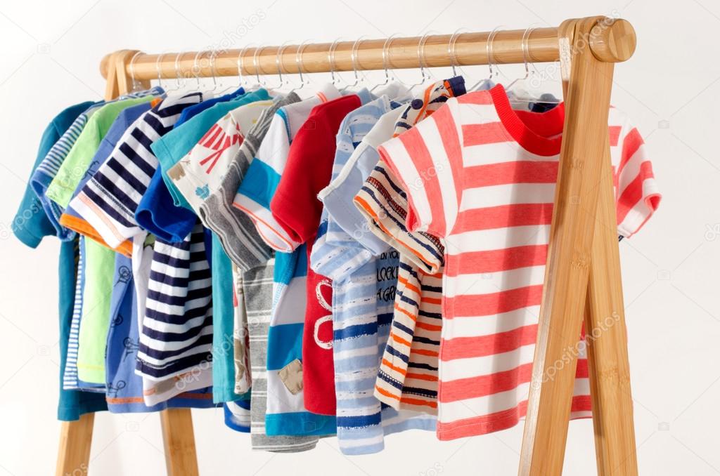 Dressing closet with clothes arranged on hangers.Colorful wardrobe of newborn,kids, toddlers, babies full of all clothes.Many t-shirts,pants, shirts,blouses, onesie hanging