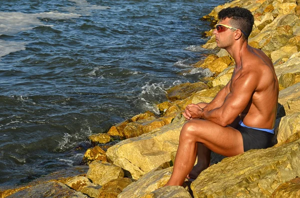 Strong bodybuilder with six pack.Fitness trainer with perfect abs, shoulders,biceps, triceps,chest, flexing his muscles on the beach with sea waves on the background, training in vacation — Stockfoto