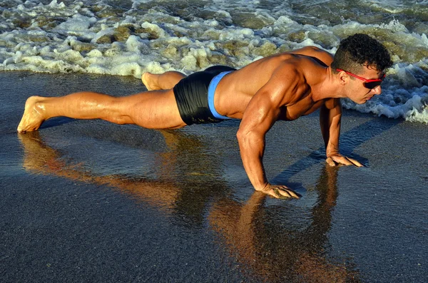 Strong bodybuilder with six pack.Fitness trainer with perfect abs, shoulders,biceps, triceps,chest, flexing his muscles on the beach, training in vacation, doing push ups in the sand — Stockfoto