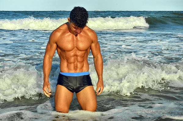 Bodybuilder fort avec six pack.Fitness entraîneur avec abdos parfaits, épaules, biceps, triceps, poitrine, fléchissant ses muscles sur la plage avec des vagues de mer sur le fond, l'entraînement en vacances — Photo