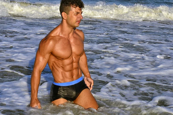 Forte bodybuilder con sei pacchetti.Fitness trainer con addominali perfetti, spalle, bicipiti, tricipiti, petto, flettendo i muscoli sulla spiaggia con onde marine sullo sfondo, allenamento in vacanza — Foto Stock