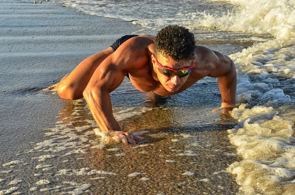 Strong bodybuilder with six pack.Fitness trainer with perfect abs, shoulders,biceps, triceps,chest, flexing his muscles on the beach, training in vacation, doing push ups in the sand — Stok fotoğraf