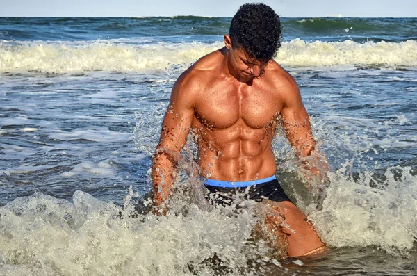 Strong bodybuilder with six pack.Fitness trainer with perfect abs, shoulders,biceps, triceps,chest, flexing his muscles on the beach with sea waves on the background, training in vacation — Zdjęcie stockowe
