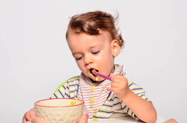 Bebé comiendo comida con una cuchara, niño pequeño comiendo desordenado y recibiendo —  Fotos de Stock