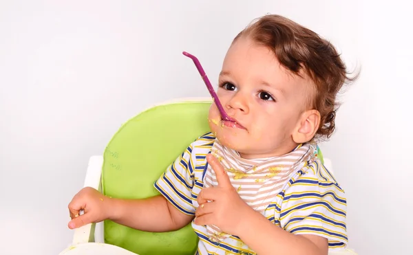 Baby eating food with a spoon, toddler eating messy and getting — Zdjęcie stockowe