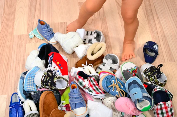 Close up on toddler legs near a lot of baby shoes. — Stock Photo, Image
